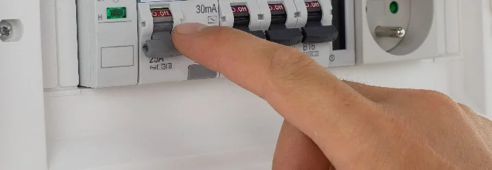 Eine Hand schaltet einen Sicherungsautomaten in einem Sicherungskasten aus.